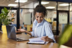 Jovem analisando documentos ao lado do notebook, demonstrando organização e foco, exemplo de o que é proatividade no dia a dia