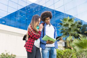 Dois estudantes em frente a prédio universitário consultando material de estudos, representando a experiência acadêmica na Uninter.
