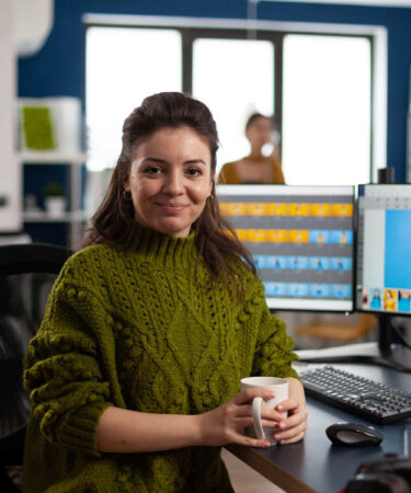 Mulher trabalhando em um escritório, segurando uma caneca enquanto edita imagens em softwares de design, cenário ideal para quem busca um curso de Design Gráfico.