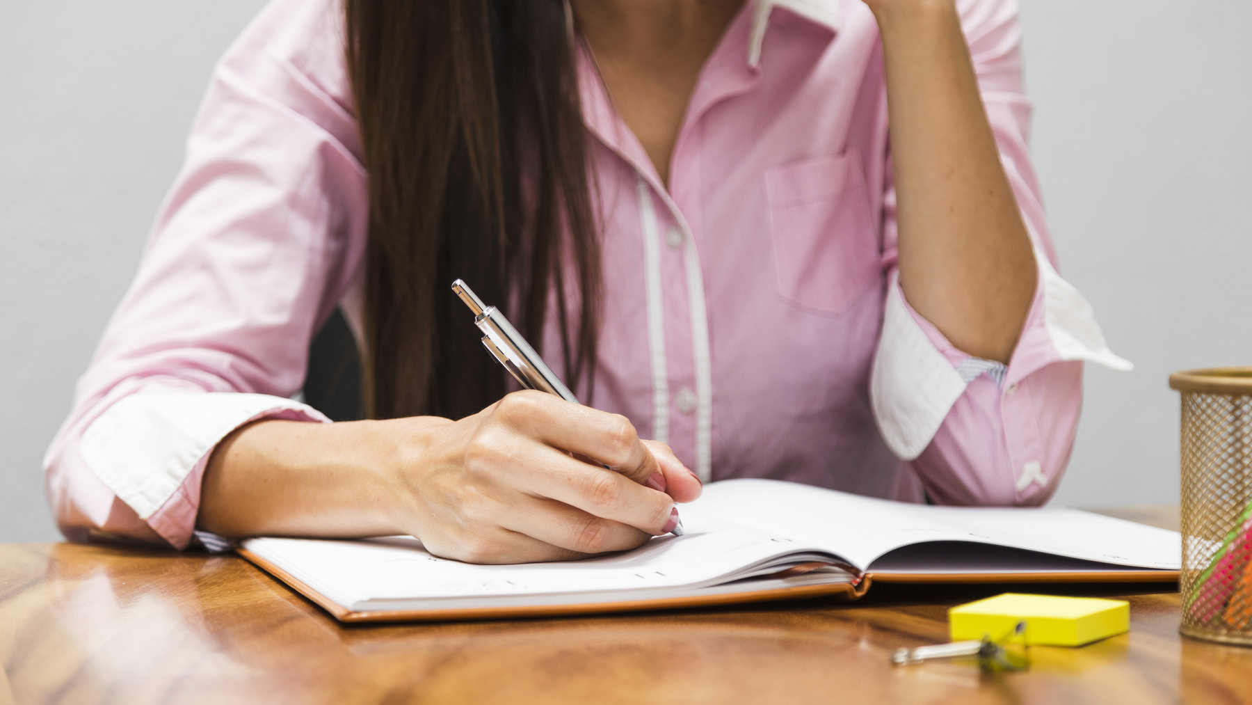 Mulher anotando ideias em um caderno sobre a mesa, simbolizando como fazer um artigo de opinião de forma organizada.
