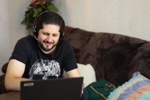 homem adulto sorridente, praticando o lifelong learning sentado em um sofá com um notebook a sua frente.
