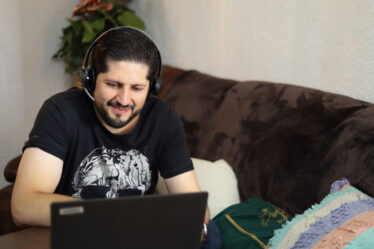 homem adulto sorridente, praticando o lifelong learning sentado em um sofá com um notebook a sua frente.
