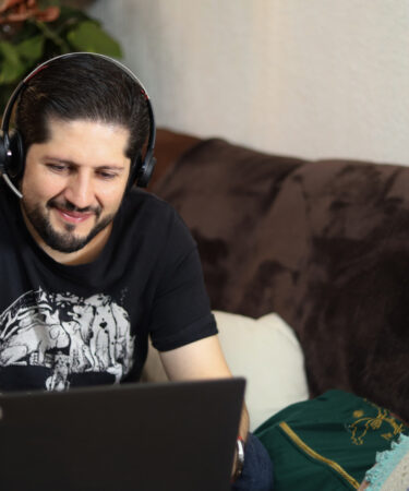homem adulto sorridente, praticando o lifelong learning sentado em um sofá com um notebook a sua frente.