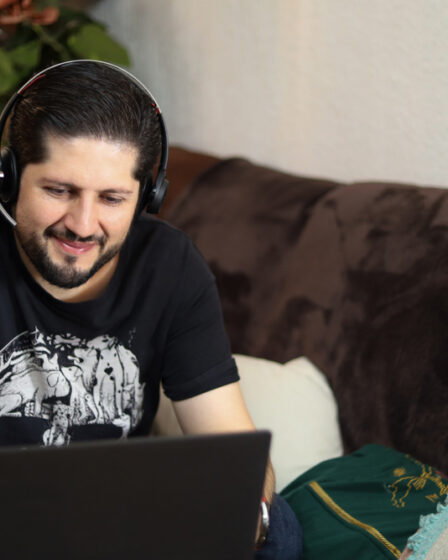 homem adulto sorridente, praticando o lifelong learning sentado em um sofá com um notebook a sua frente.