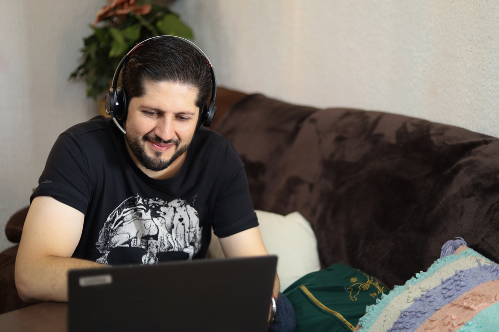 homem adulto sorridente, praticando o lifelong learning sentado em um sofá com um notebook a sua frente.