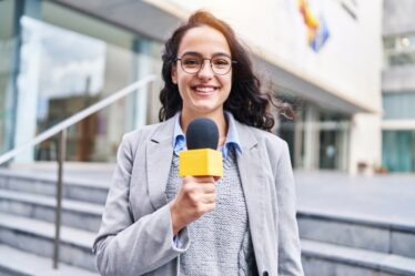 Mulher jornalista com microfone trabalhando em ambiente externo.