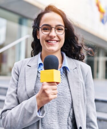Mulher jornalista com microfone trabalhando em ambiente externo.