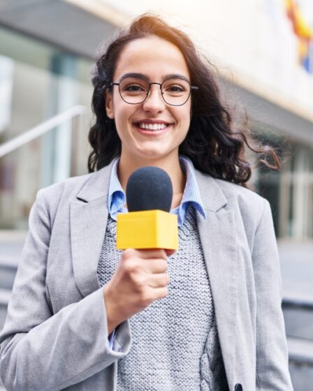 Mulher jornalista com microfone trabalhando em ambiente externo.