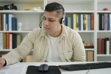 Jovem estudante em chamada de vídeo, fazendo anotações sobre o ikigai, em uma biblioteca.
