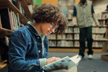 Estudante na biblioteca lendo livro durante sua preparação para o Enem.