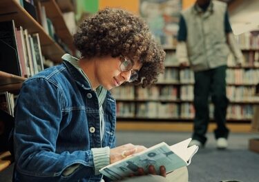 Estudante na biblioteca lendo livro durante sua preparação para o Enem.
