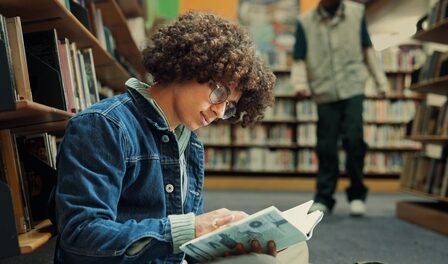 Estudante na biblioteca lendo livro durante sua preparação para o Enem.