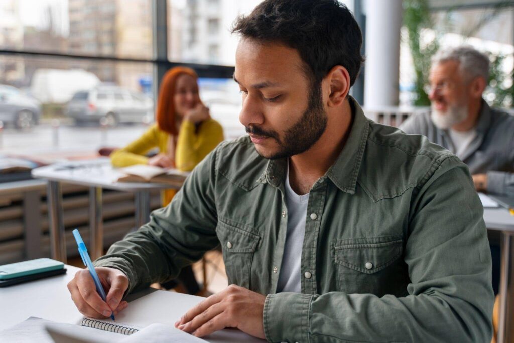 Homem escrevendo em caderno durante momento de estudos, ilustrando o que é vestibular e a dedicação necessária para conquistar uma vaga no ensino superior.