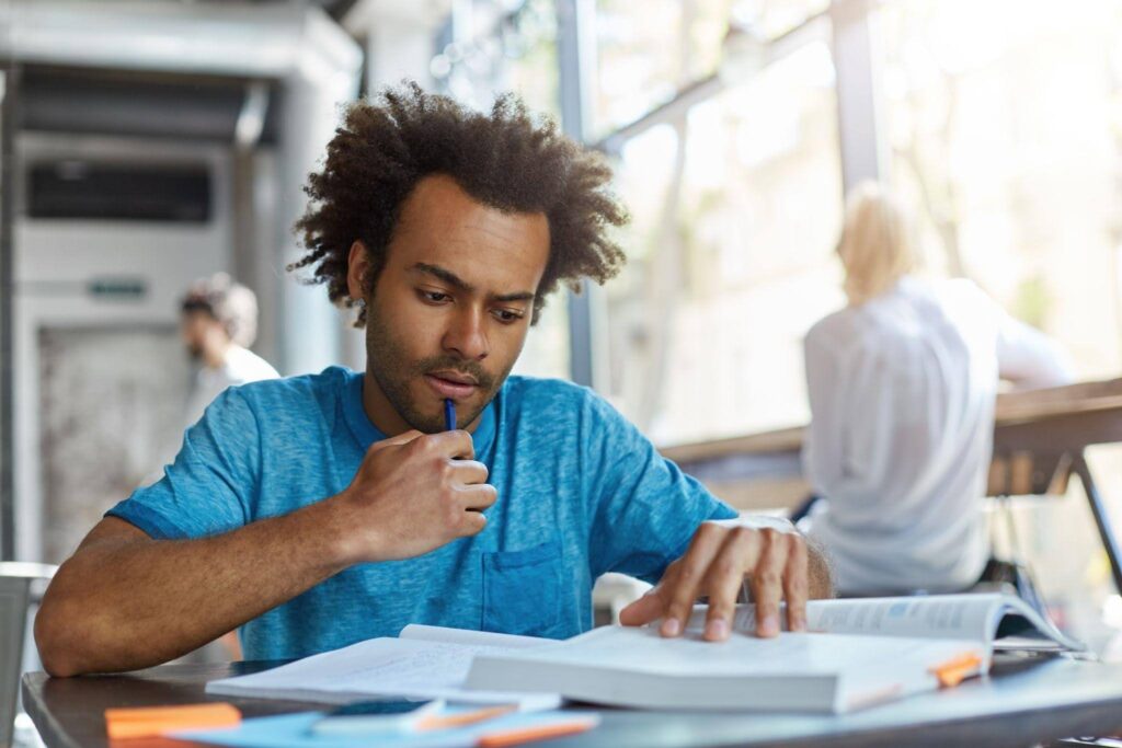 Estudante concentrado lendo livros e fazendo anotações, representando o que é vestibular e a rotina de preparação para provas e ingresso na faculdade.