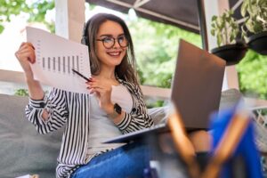 Mulher trabalhando em home office com notebook e gráficos financeiros, demonstrando como as Ciências Contábeis se aplicam à gestão e à análise de resultados