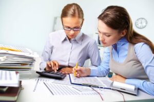 Profissionais analisando relatórios financeiros e usando calculadora em escritório, representando o que é Ciências Contábeis e a rotina da área contábil.