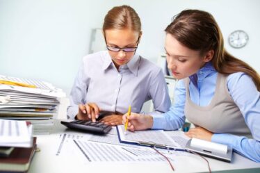 Profissionais analisando relatórios financeiros e usando calculadora em escritório, representando o que é Ciências Contábeis e a rotina da área contábil.