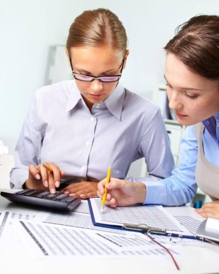 Profissionais analisando relatórios financeiros e usando calculadora em escritório, representando o que é Ciências Contábeis e a rotina da área contábil.