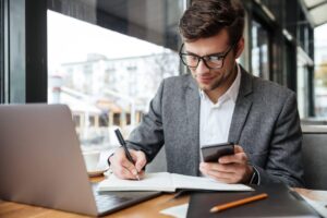 Homem pesquisando e fazendo anotações sobre qual a diferença entre MBA e pós-graduação.