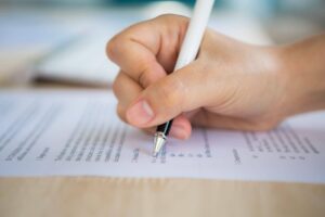 Close nas mãos de uma pessoa escrevendo em documento de inscrição, relacionado ao tema da inscrição no Enem e à preparação para o exame.