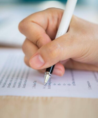 Close nas mãos de uma pessoa escrevendo em documento de inscrição, relacionado ao tema da inscrição no Enem e à preparação para o exame.