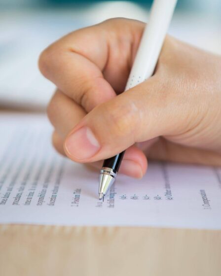 Close nas mãos de uma pessoa escrevendo em documento de inscrição, relacionado ao tema da inscrição no Enem e à preparação para o exame.