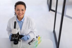 Mulher utiliza microscópio e tubos de ensaio, representando o que é Biomedicina e suas áreas de atuação.