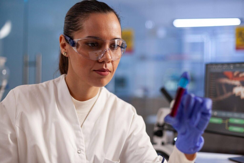 Biomédica observa tubo de ensaio durante análise clínica em laboratório, exemplificando o que é Biomedicina na área da saúde.