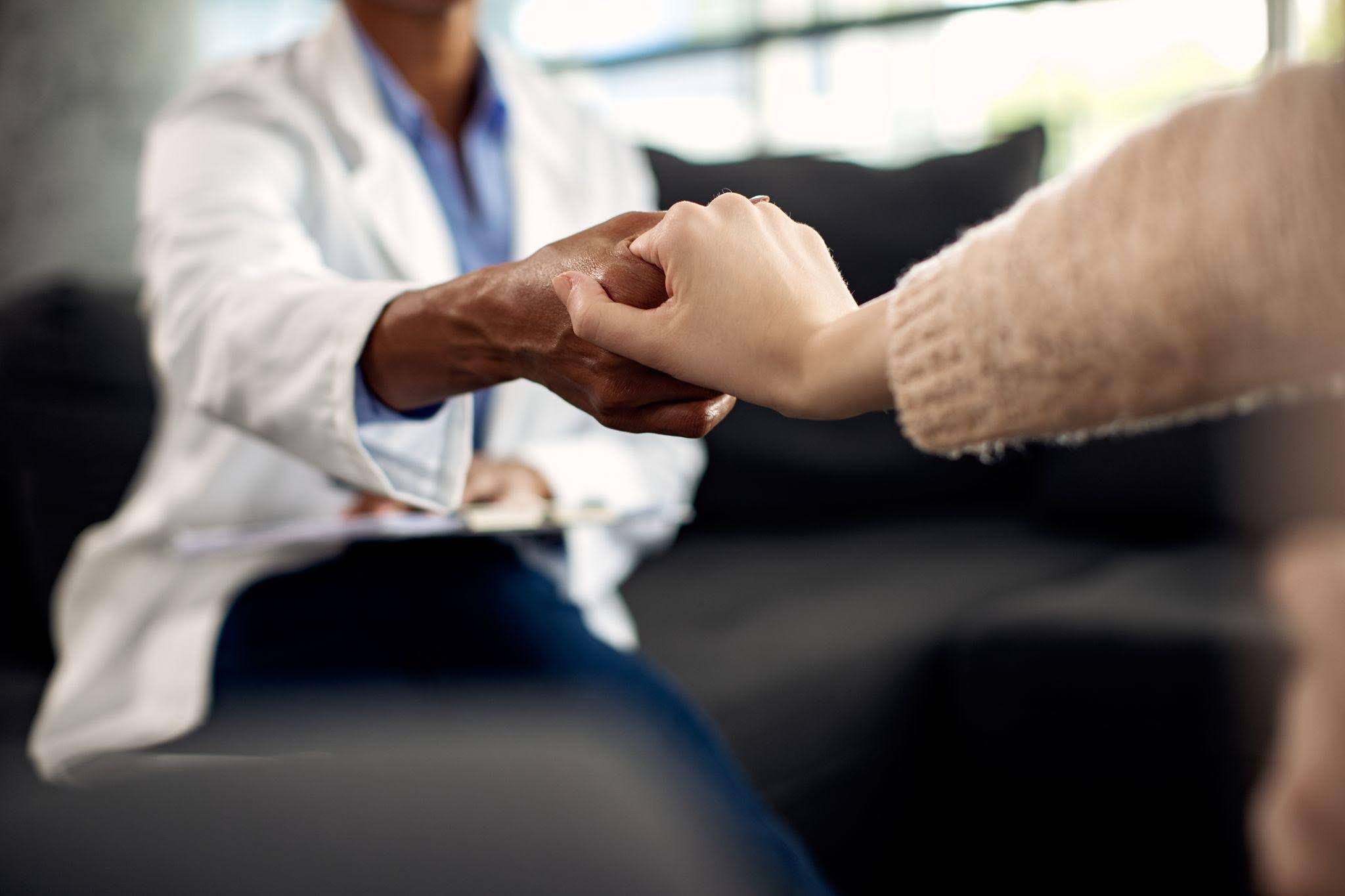 Psicólogo clínico segura a mão de uma paciente durante uma consulta, transmitindo acolhimento, empatia e apoio emocional.