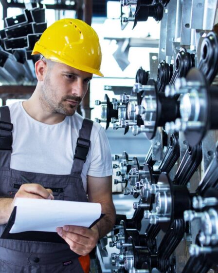 Especialista em Engenharia de Produção inspecionando componentes industriais e registrando informações para controle de qualidade em ambiente fabril.
