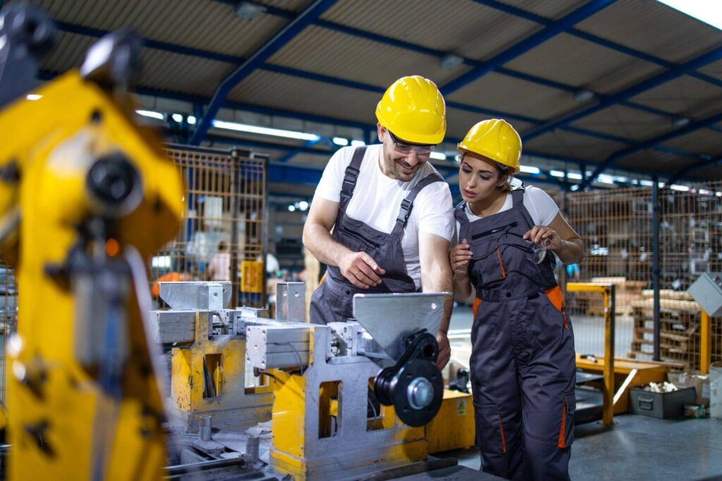 Dois profissionais da Engenharia de Produção inspecionando uma máquina industrial em uma fábrica.
