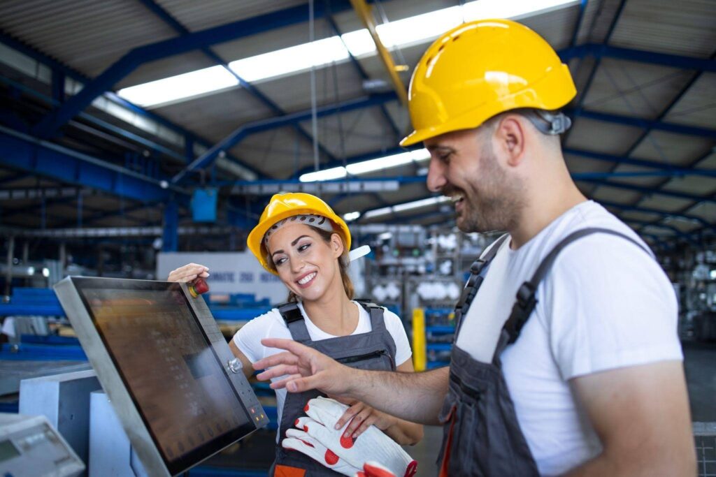 Dois profissionais com capacetes de segurança operando painel de controle industrial.