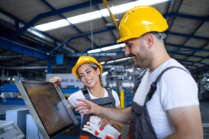 Dois profissionais com capacetes de segurança operando painel de controle industrial.