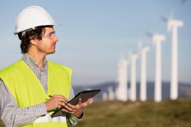 Especialista em engenharia ambiental realizando inspeção em parque eólico com tablet, monitorando o desempenho de turbinas para produção sustentável de energia.