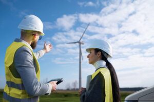 Profissionais de Engenharia Ambiental inspecionando turbina eólica em parque de energia renovável durante avaliação técnica.