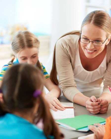 Professora acompanha crianças durante uma atividade em equipe, representando competências desenvolvidas na Licenciatura em Pedagogia.