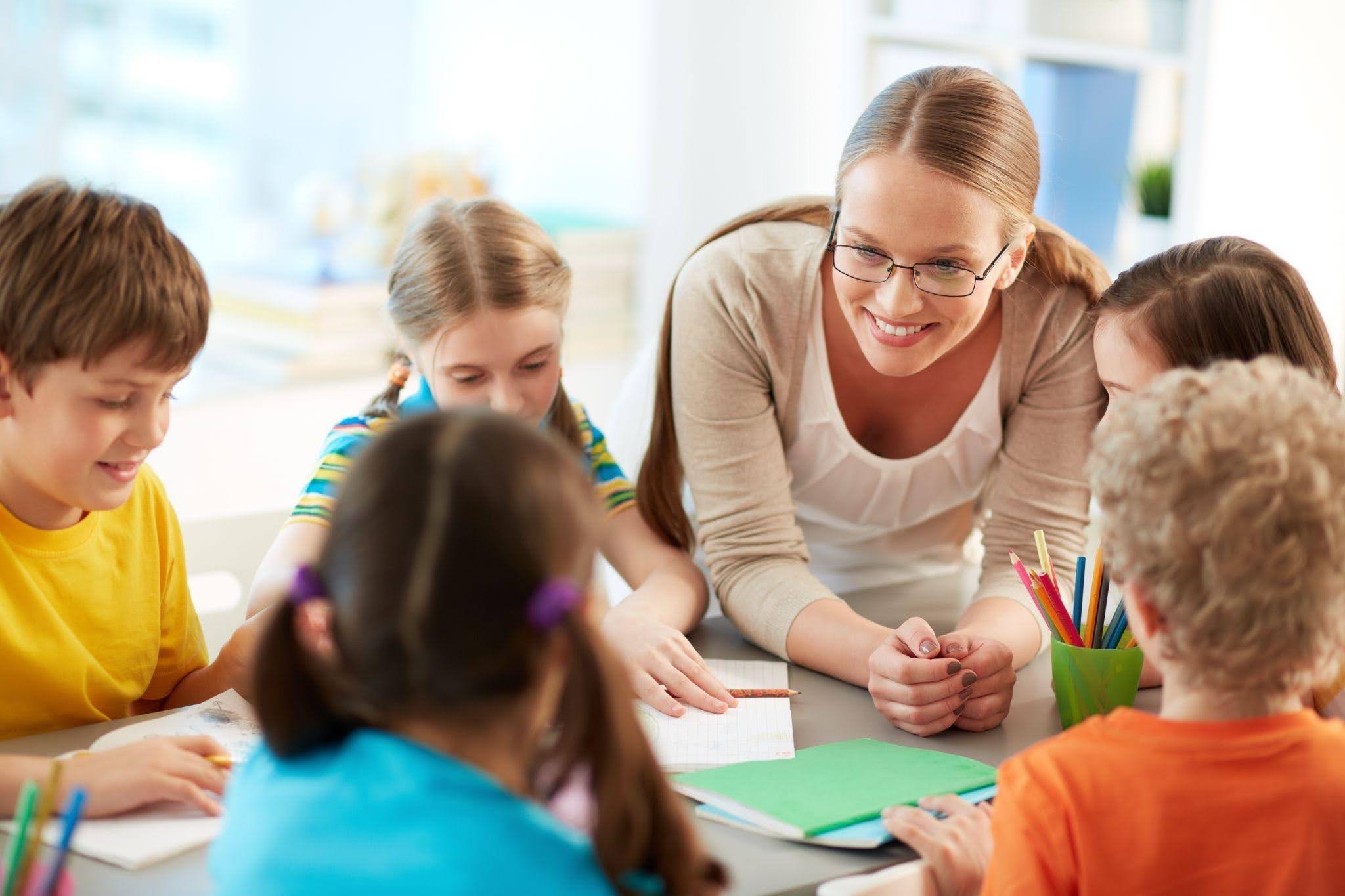 Professora acompanha crianças durante uma atividade em equipe, representando competências desenvolvidas na Licenciatura em Pedagogia.