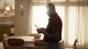 Vô Carlos, personagem da novelinha da Uninter O Próximo Passo observa um diploma em casa, próximo a uma janela iluminada.