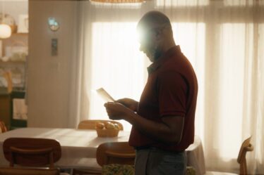 Vô Carlos, personagem da novelinha da Uninter O Próximo Passo observa um diploma em casa, próximo a uma janela iluminada.