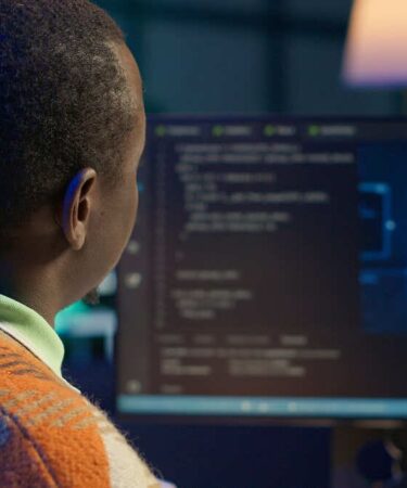 Homem trabalhando em computador com códigos de programação e imagem de inteligência artificial na tela.