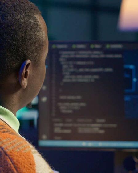 Homem trabalhando em computador com códigos de programação e imagem de inteligência artificial na tela.
