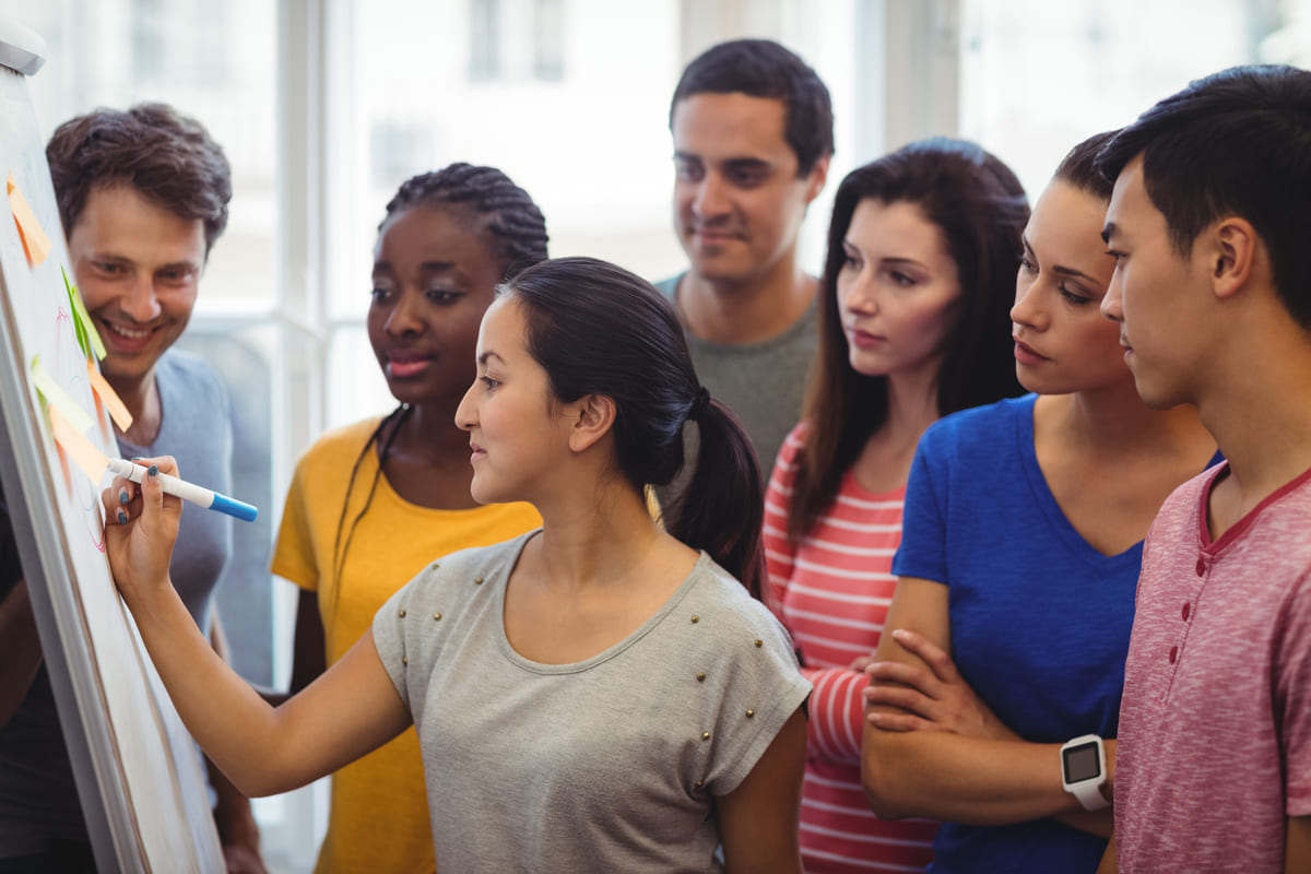 Estudantes reunidos em frente a um quadro colaborando em uma atividade em grupo, ilustrando o aprendizado de Sociologia por meio da troca de conhecimentos.