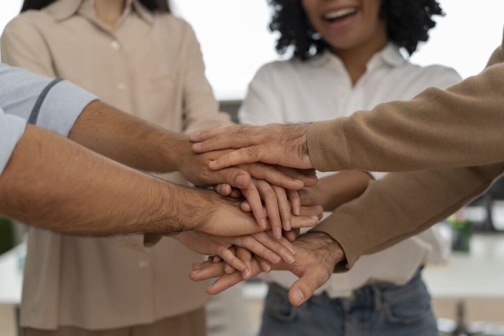 Pessoas com as mãos umas sobre as outras em um gesto de união e trabalho em equipe, representando a área de Serviço Social e a colaboração coletiva.