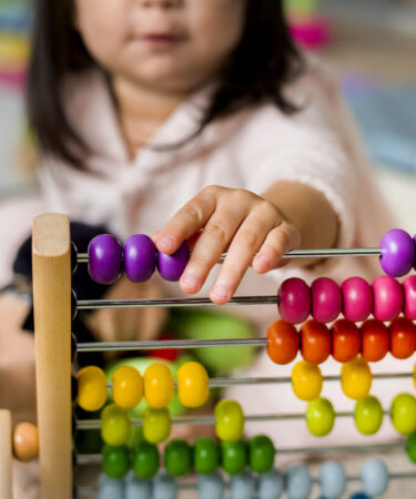 Criança brincando com ábaco colorido para aprender a contar e desenvolver habilidades matemáticas.