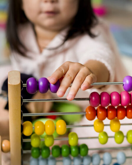 Criança brincando com ábaco colorido para aprender a contar e desenvolver habilidades matemáticas.