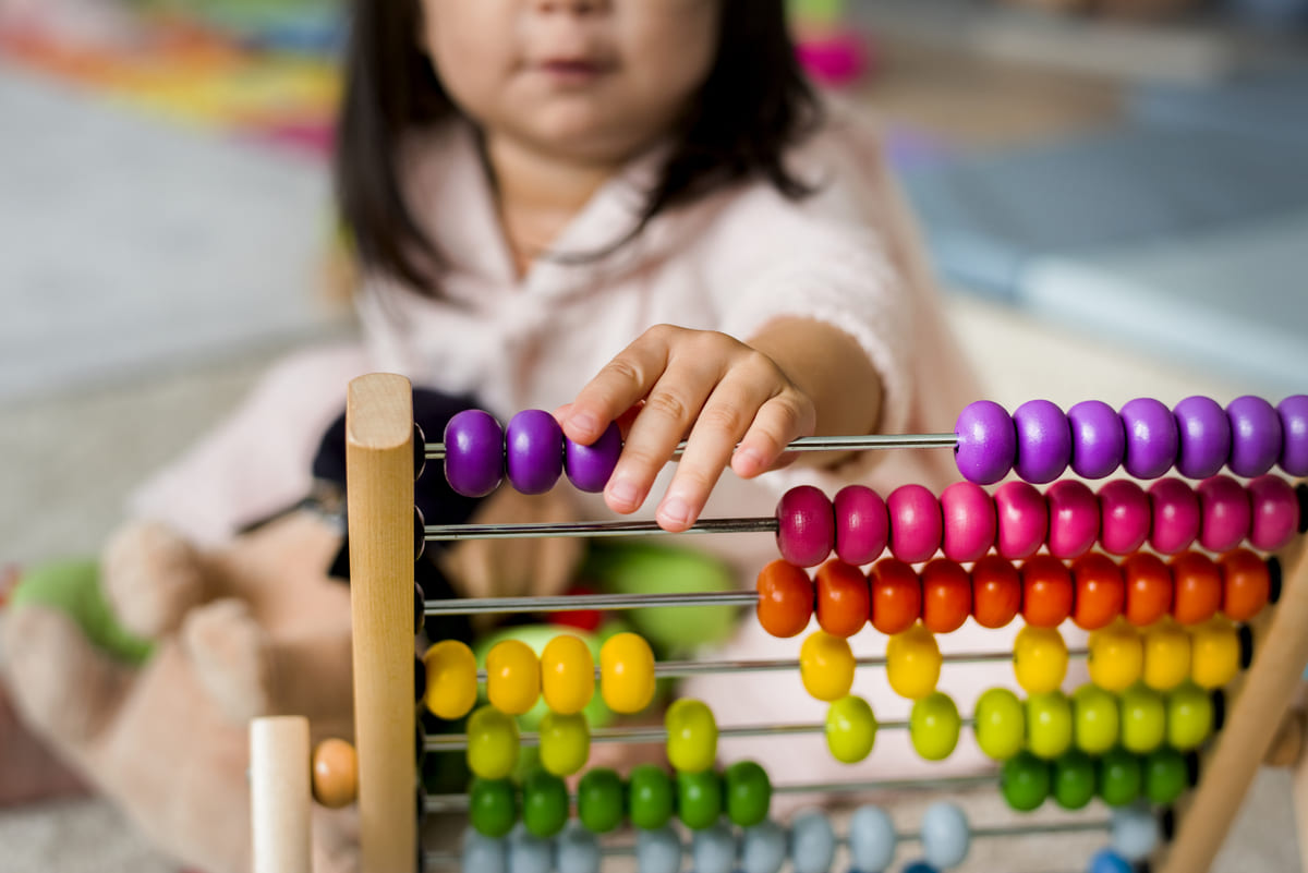 Criança brincando com ábaco colorido para aprender a contar e desenvolver habilidades matemáticas.