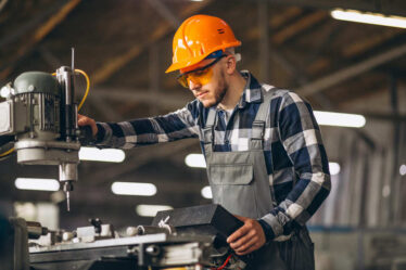 Profissional da Engenharia de Fabricação Mecânica operando máquina-ferramenta com equipamentos de proteção individual em ambiente de manufatura industrial.