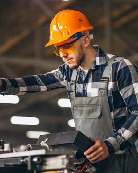 Profissional da Engenharia de Fabricação Mecânica operando máquina-ferramenta com equipamentos de proteção individual em ambiente de manufatura industrial.