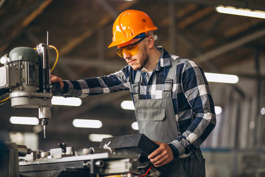 Profissional da Engenharia de Fabricação Mecânica operando máquina-ferramenta com equipamentos de proteção individual em ambiente de manufatura industrial.