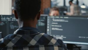 Desenvolvedor trabalhando em frente a monitores com código em ambiente corporativo, demonstrando atividades de Engenharia de Software para Dispositivos Móveis.